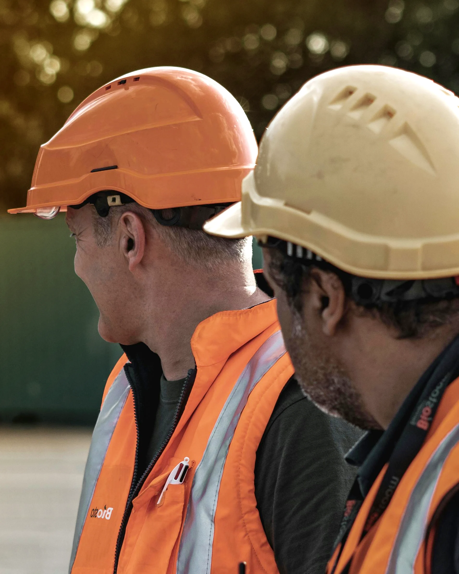 Two construction workers with safety gear in the foreground, and looking to the right away from the camera