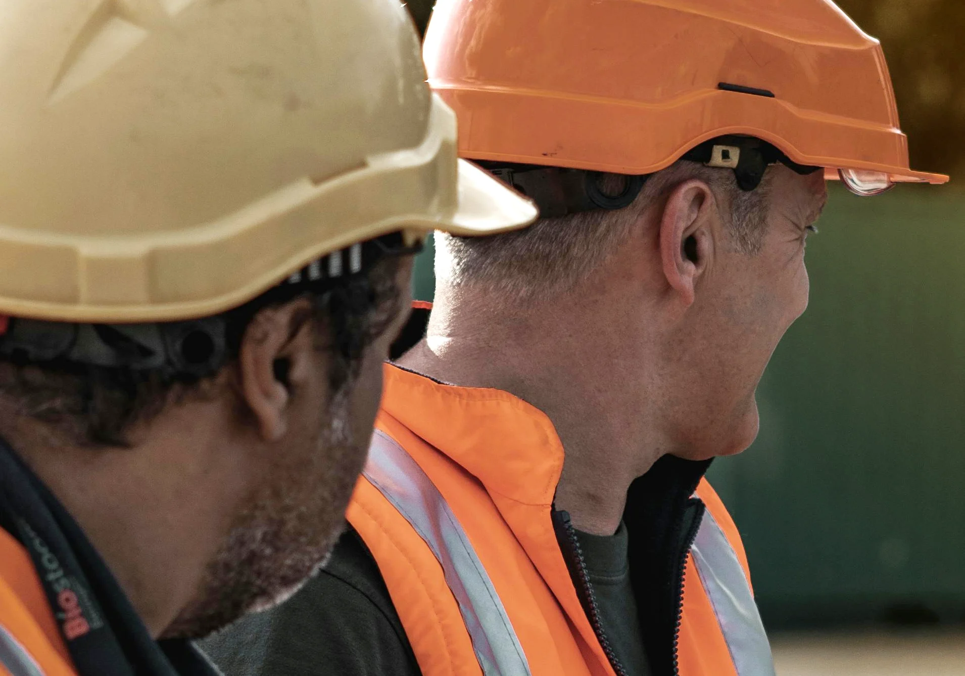 Two construction workers with safety gear in the foreground, and looking to the right away from the camera